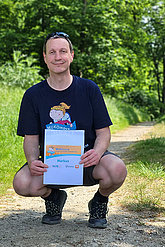 Mann posiert in der Hocke mit MUKOmove-Startnummer und MUKOmove-T-Shirt