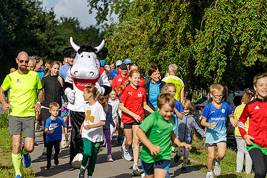 Impression vom Blocky Block Spendenlauf Viele Kinder und ein Maskottchen in Form einer Kuh laufen im Grünen.