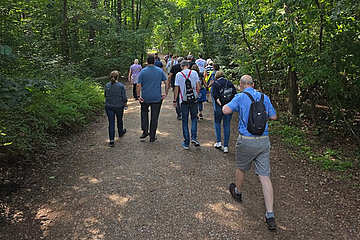 Gruppe von Menschen auf einem Waldweg, um sie herum sind Laubbäume.