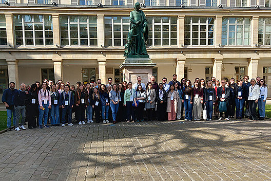Gruppenfoto von etwa 40 Personen vor einem historisch aussehenden Gebäude mit einer Bronzestatue