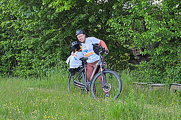 Frau mit großem Stoffpinguin auf dem Fahrrad - beide mit MUKOmove-T-Shirts