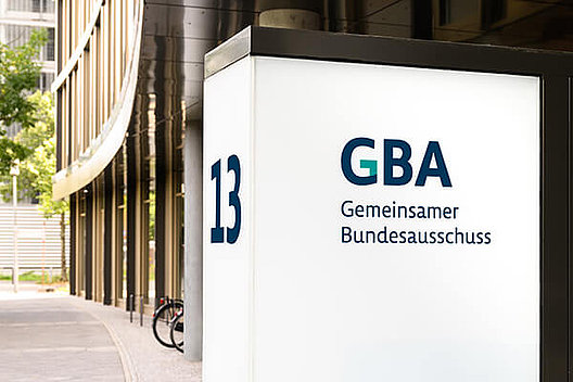 Gemeinsamer Bundesausschuss Außenansicht Großes Gebäude, im Mittelpunkt des Bildes ist aber ein Schild, auf dem "Gemeinsamer Bundesausschuss" zu lesen ist.