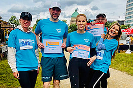 Vier Menschen in blauen Lauf-Shirts posieren mit MUKOmove-Startnummern für die Kamera. 