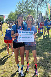 Zwei Frauen in Laufkleidung posieren mit MUKOmove-Schild. Sie waren beim Regensburger Halbmarathon für den MUKOmove dabei. 
