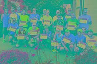 Größere Gruppe posiert mit MUKOmove-Startnummer draußen, viele von ihnen haben rote T-Shirts an.