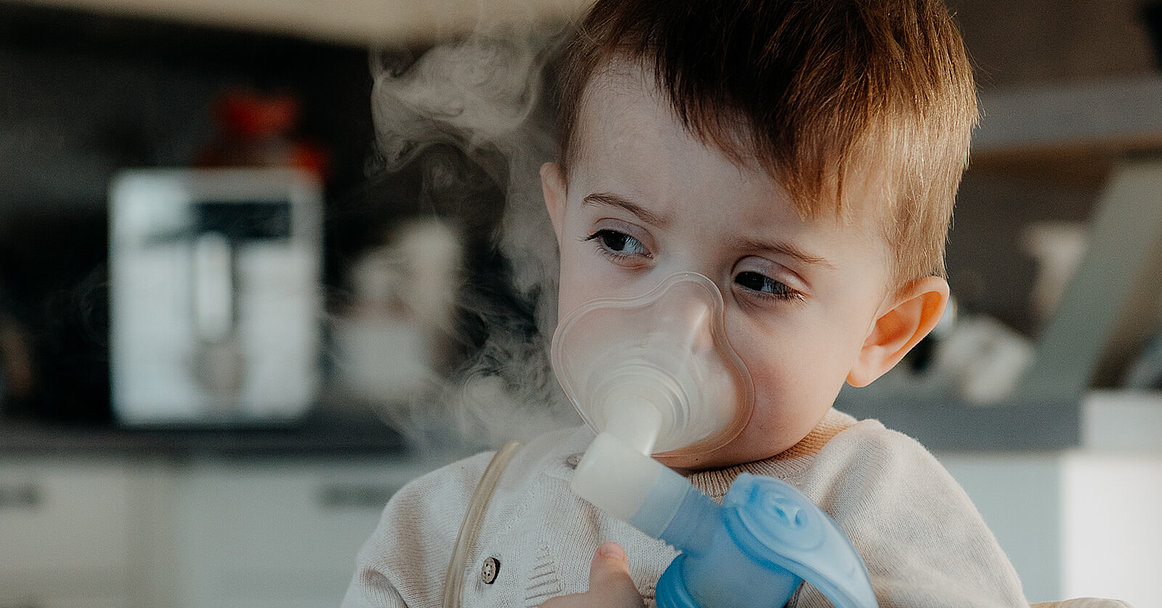 Zweijähriger Junge mit Inhaliergerät - man sieht Wasserdampf aufsteigen. 