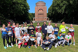 Eine Schulklasse steht auf einer Wiese vor einem Denkmal, alle halten MUKOmove-Startnummern in der Hand. 