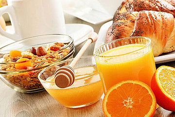 Blick auf ein Frühstücksbüffet im Hotel. Man sieht Orangensaft, Honig, Obst und vieles mehr. 