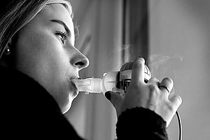 Frau inhaliert am Fenster. Inhalieren gehört zur Standard-Therapie bei Mukoviszidose. 