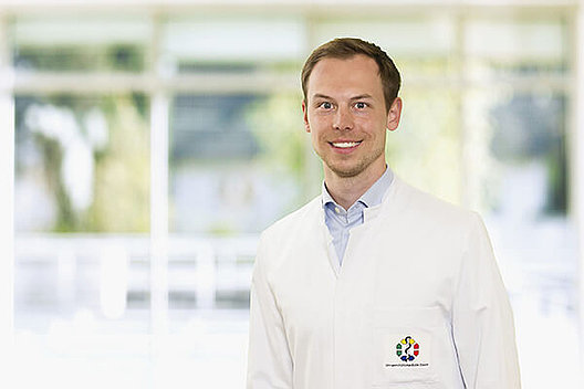 PD Dr. med. Marcel Opitz untersucht die kardiovaskulären und metabolischen Risiken einer CFTR-Modulatortherapie bei erwachsenen Patienten. PD Dr. med. Marcel Opitz im Labor. Er trägt einen weißen Kittel über einem hellblauen Hemd. Foto: Mukoviszidose e.V.