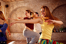 Junge Frauen in Tank-Tops tanzen vor einer aus Stein gemauerten Wand.
