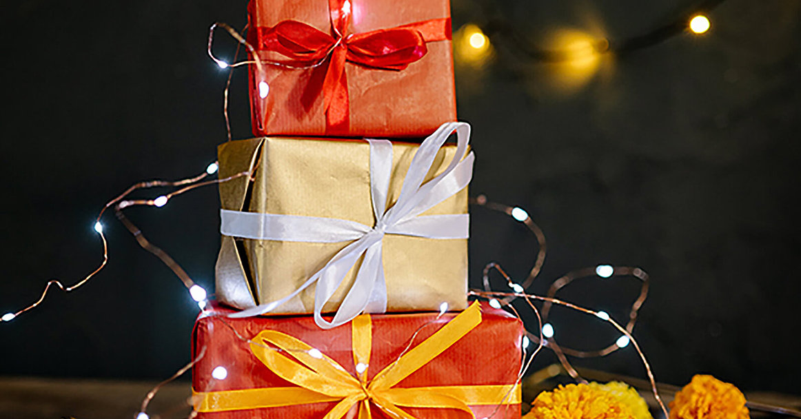 Weihnachtsgeschenke in orangenem Papier aufeinandergestapelt vor einem schwarzen Hintergrund