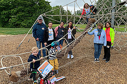 Eltern und Kinder haben sich an einer Kletterspinne auf dem Spielplatz versammelt. Viele von ihnen haben Startnummern vom MUKOmove angepinnt. Es sind auch mehrere kleine Kinder dabei. 