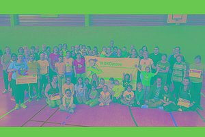 Große Gruppe Menschen (Kinder und Erwachsene) in der Turnhalle mit MUKOmove-Banner