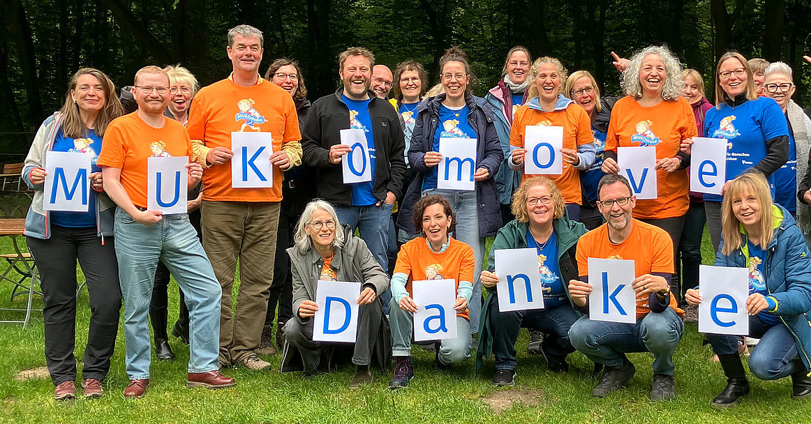 Eine Gruppe von Menschen mit MUKOmove-T-Shirts hält die Buchstaben "MUKOmove Danke" hoch. 
