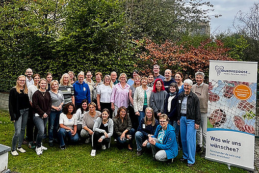 Gruppenbild von der Selbsthilfetagung in Münster Gruppenbild vor Bäumen, rund 35 Menschen (Männer und Frauen) posieren mit einem Roll-Up des Mukoviszidose e.V.