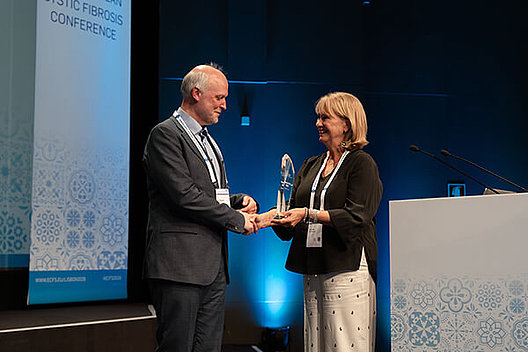 Lutz Nährlich erhält den European Cystic Fibrosis Society Award. Eine Frau übergibt einem Mann auf einer Bühne einen Preis.