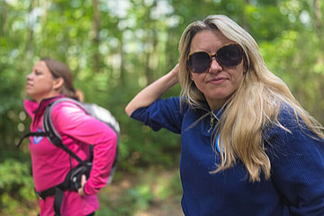 Zwei Frauen im Wald, eine davon (blond, im Vordergrund) schaut in die Kamera. 