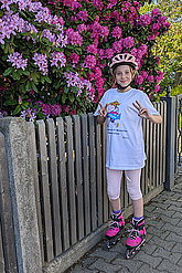 Mädchen mit MUKOmove-Shirt und Inlinern vor rosa-blühenden Büschen