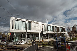 Außenansicht des Congress Centrums Würzburg, im Hintergrund sieht man dunkele Wolken und etwas blauen Himmel. 