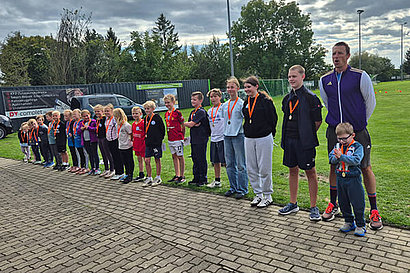 Viele Kinder unterschiedlichen Alters stehen auf einem Sportplatz in einer Reihe.