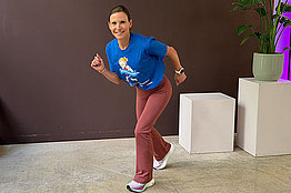 Frau mit MUKOmove-T-Shirt im Lauf-Stellung vor einer brauen Wand