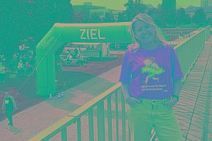 Frau mit orangenem MUKOmove-T-Shirt, in Hintergrund sieht man den Zieleinlauf für eine Laufveranstaltung
