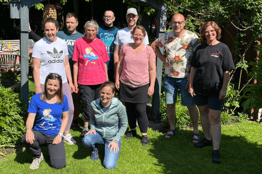 Gruppe mit MUKOmove-T-Shirts draußen im Grünen, die Sonne scheint. 