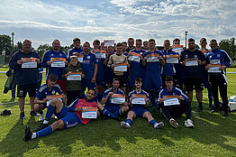 Eine Fußballmannschaft mit vorwiegend blauen Trikots posiert auf dem Fußballfeld mit MUKOmove-Startnummern. 