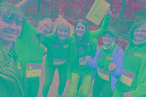 Eine Gruppe von Frauen in Sportkleidung, sie tragen MUKOmove-Startnummern und halten ein MUKOmove Schild in die Luft. Im Hintergrund sieht man Bäume. 