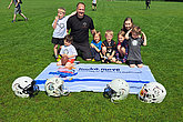 MUKOmove-Banner liegt im Gras, davor liegen Football-Helme, dahinter sind Kinder und Erwachsene zu sehen. 