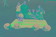 MUKOmove-Banner liegt im Gras, davor liegen Football-Helme, dahinter sind Kinder und Erwachsene zu sehen. 