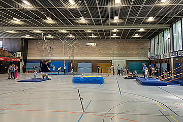 Blick in die Turnhalle bei der Kinder-Olympiade, man sieht Kinder, viele Matten und viele Spielgeräte. 