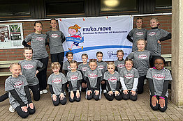 Gruppe von Menschen - auch Kinder - mit grauen T-Shirts posieren vor einem MUKOmove-Banner