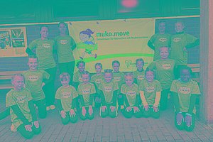 Gruppe von Menschen - auch Kinder - mit grauen T-Shirts posieren vor einem MUKOmove-Banner