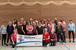 Eine Gruppe von Menschen posiert in einer Turnhalle mit MUKOmove-Banner