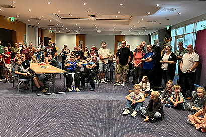 Menschen und Kinder sitzen in einem Raum und schauen zur Bühne.