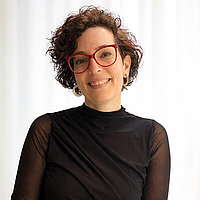 Beatriz Dirksen Porträt einer Frau mit kurzen, dunklen, lockigen Haaren, Brille, schwarzem Oberteil