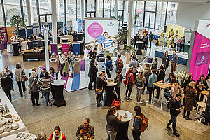 Von oben geschossenes Foto, man sieht viele Menschen in einer Halle mit Informationsständen von Unternehmen der gesundheitsbezogenen Industrie. Blick in die Industrieausstellung der Deutschen Mukoviszidose Tagung. 