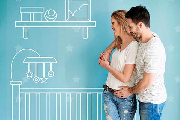 Ein Pärchen umarmt sich vor und schaut dabei auf eine türkise Wand, auf der ein Kinderbett aufgemalt ist. 