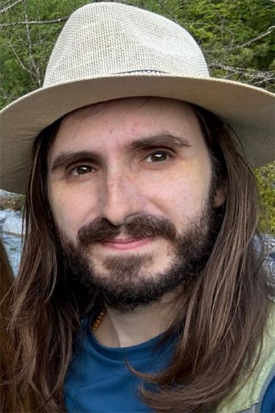 Porträt eines Mannes mit Strohhut, längeren braunen Haaren und mittellangem Bart